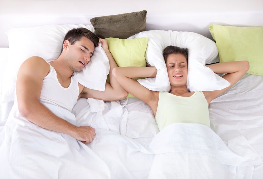 Man snoring, woman covering ears with pillow