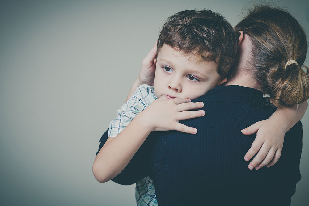 Mother holding sad boy against her shoulder