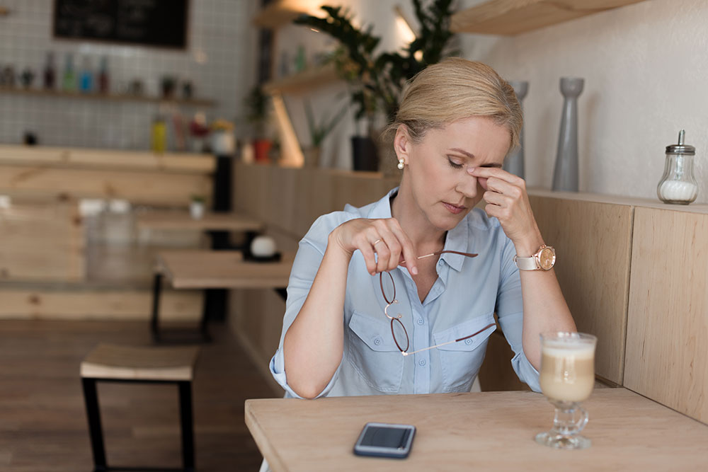 A tired middle aged woman sitting at a table with a coffee cup and cellphone in front of her