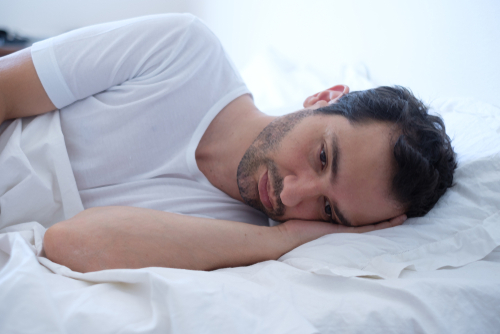 man wearing a white shirt laying in bed awake and worried