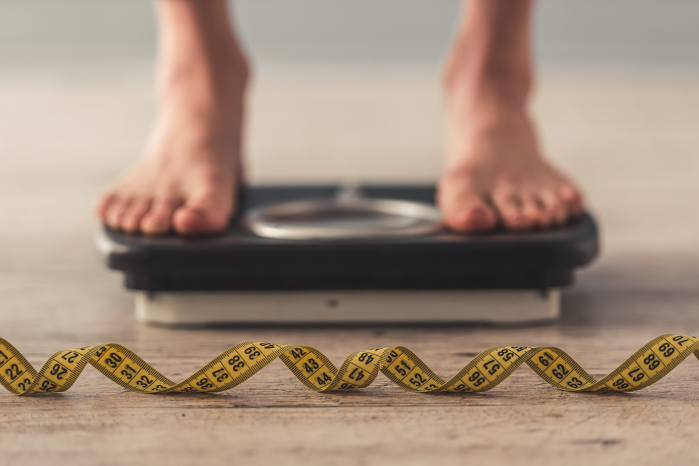 person standing on scale with a measuring tape in the foreground