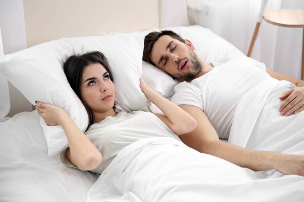 Man snoring while an annoyed woman tries to sleep